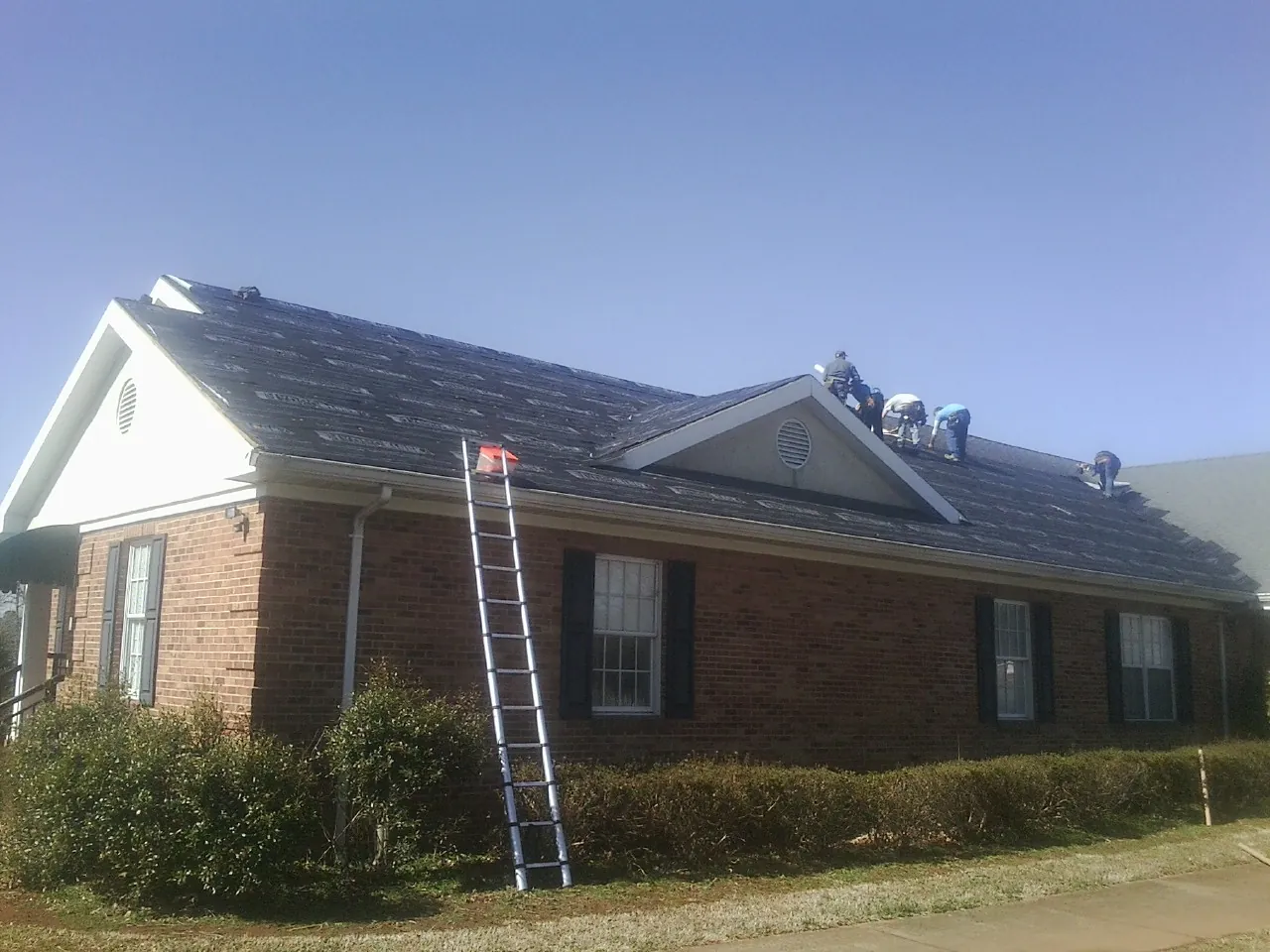 Crew tearing shingles off a brick ranch roof with a ladder set — Metal Roof Repair work by our crew in Fall City