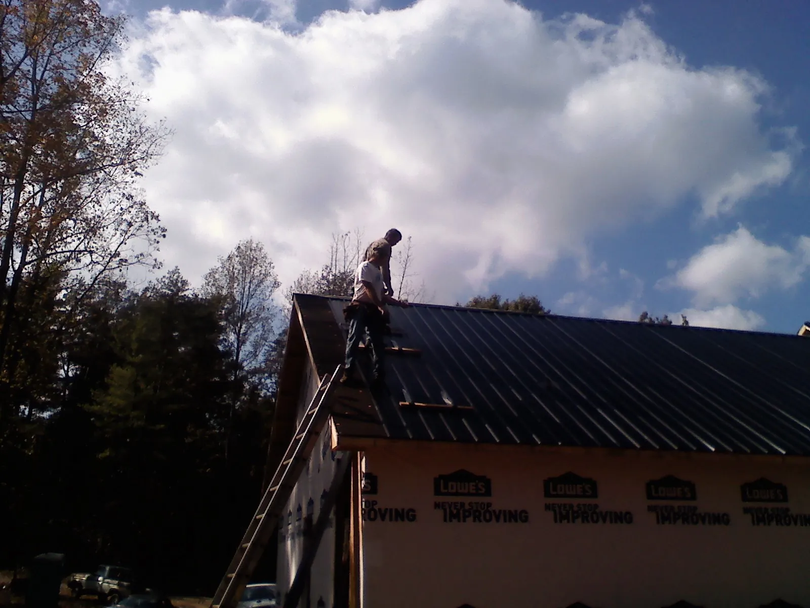 Roofer fastening dark metal panels high against a cloudy sky, from a Roof Inspection job in Fall City