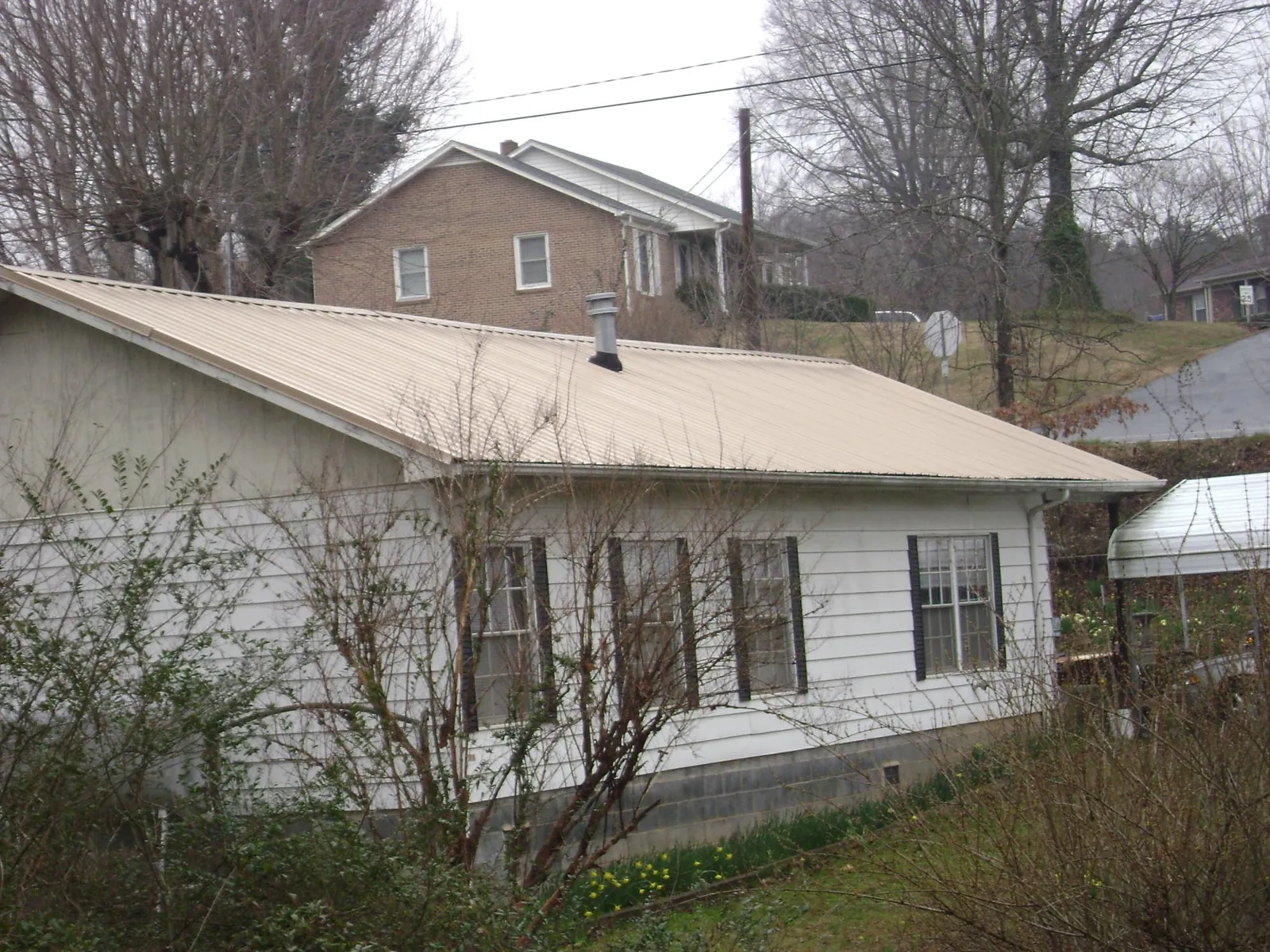 Tan metal roof on a white sided house set into a hillside — Commercial Roofing by Roofing Brothers in Fall City
